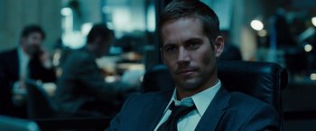 Movie still from “Fast & Furious” (2009), directed by Justin Lin – A man in a suit and tie sitting in a chair; Close Up shot, Over the shoulder angle