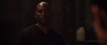 Movie still from “Fast Five” (2011), directed by Justin Lin – A man in a black shirt is standing in a dark room; Close Up shot, Over the shoulder angle