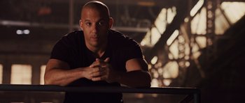 Movie still from “Fast Five” (2011), directed by Justin Lin – A bald man leaning on a wall with his hands crossed; Close Up shot, Over the shoulder angle