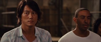 Movie still from “Fast Five” (2011), directed by Justin Lin – A man sitting next to another man in front of a building; Close Up shot, Over the shoulder angle