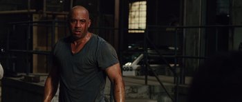 Movie still from “Fast Five” (2011), directed by Justin Lin – A man with a bruised face standing next to a building; Medium shot, Over the shoulder angle