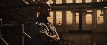 Movie still from “Fast Five” (2011), directed by Justin Lin – A man standing with his arms crossed in front of a building; Medium shot, Low angle