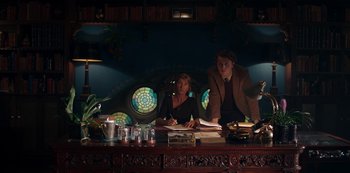 Movie still from “Fate: The Winx Saga” (2021), created by Brian Young – A man and a woman sitting in front of a desk; Medium shot, Low angle