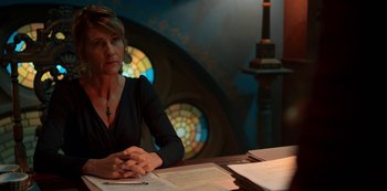 Movie still from “Fate: The Winx Saga” (2021), created by Brian Young – A woman sitting at a table in front of papers; Medium shot, Over the shoulder angle