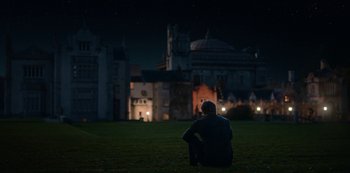 Movie still from “Fate: The Winx Saga” (2021), created by Brian Young – A man sitting on the grass in front of a castle; Extreme Wide shot, Low angle