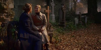 Movie still from “Fate: The Winx Saga” (2021), created by Brian Young – Two women sitting on a bench in front of a cemetery; Medium shot, Over the shoulder angle