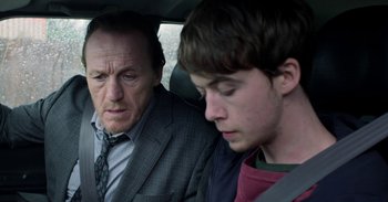 Movie still from “Black Mirror” (2011), created by Charlie Brooker – A man and a boy in the back seat of a car; Close Up shot, Over the shoulder angle