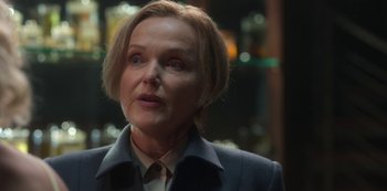 Movie still from “Fate: The Winx Saga” (2021), created by Brian Young – An older woman with blonde hair wearing a suit; Close Up shot, Over the shoulder angle