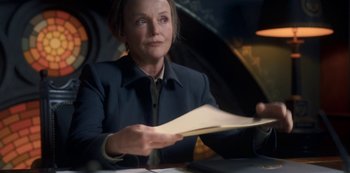 Movie still from “Fate: The Winx Saga” (2021), created by Brian Young – A woman sitting at a table holding a piece of paper; Medium shot, Over the shoulder angle