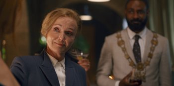 Movie still from “Fate: The Winx Saga” (2021), created by Brian Young – A woman in a business suit holding a glass of wine; Close Up shot, Over the shoulder angle
