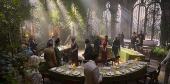 Movie still from “Fate: The Winx Saga” (2021), created by Brian Young – A group of people standing around a table with plates of food on top of it; Wide shot, High angle