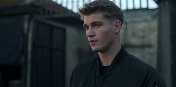 Movie still from “Fate: The Winx Saga” (2021), created by Brian Young – A young man in a black jacket looking to his left; Close Up shot, Over the shoulder angle