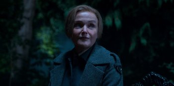 Movie still from “Fate: The Winx Saga” (2021), created by Brian Young – A woman in a coat and tie standing in front of a tree; Close Up shot, Over the shoulder angle