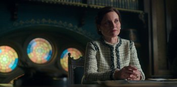 Movie still from “Fate: The Winx Saga” (2021), created by Brian Young – A woman sitting at a table in front of a stained glass window; Medium shot, Low angle