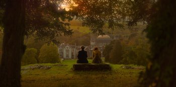 Movie still from “Fate: The Winx Saga” (2021), created by Brian Young – Two people sitting on a bench in front of a building; Extreme Wide shot, High angle