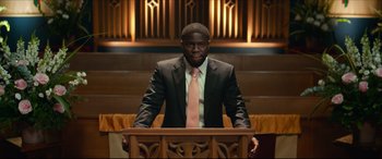 Movie still from “Fatherhood” (2021), directed by Paul Weitz – A man standing at a podium in front of an organ in a church; Medium shot, Over the shoulder angle