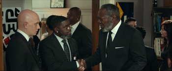 Movie still from “Fatherhood” (2021), directed by Paul Weitz – Two men in suits shaking hands in a room; Medium shot, Over the shoulder angle