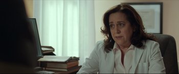 Movie still from “Fatherhood” (2021), directed by Paul Weitz – A woman sitting at a table with a stack of books; Close Up shot, Over the shoulder angle