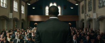 Movie still from “Fatherhood” (2021), directed by Paul Weitz – A man standing in front of a group of people; Medium shot, Over the shoulder angle