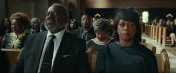 Movie still from “Fatherhood” (2021), directed by Paul Weitz – A group of people sitting in a row at a funeral; Medium shot, Low angle