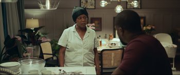 Movie still from “Fatherhood” (2021), directed by Paul Weitz – An older woman standing at a dining room table; Medium shot, Over the shoulder angle