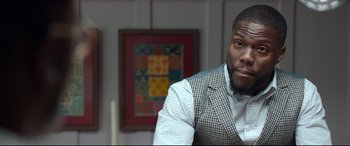 Movie still from “Fatherhood” (2021), directed by Paul Weitz – A person sitting in a chair wearing a suit; Close Up shot, Over the shoulder angle