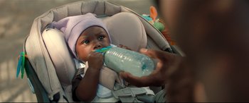 Movie still from “Fatherhood” (2021), directed by Paul Weitz – A baby is in a car seat drinking from a water bottle; Close Up shot, High angle