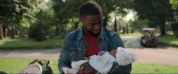 Movie still from “Fatherhood” (2021), directed by Paul Weitz – A man holding a baby in his arms outside; Medium shot, Over the shoulder angle