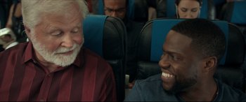 Movie still from “Fatherhood” (2021), directed by Paul Weitz – Two men sitting on a blue seat on an airplane; Close Up shot, Over the shoulder angle