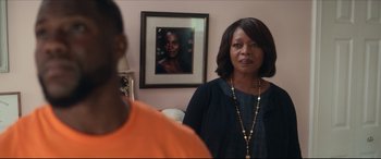 Movie still from “Fatherhood” (2021), directed by Paul Weitz – A woman standing in front of a picture of a man; Medium shot, Over the shoulder angle