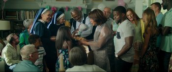 Movie still from “Fatherhood” (2021), directed by Paul Weitz – A group of people standing around a table; Medium shot, Over the shoulder angle