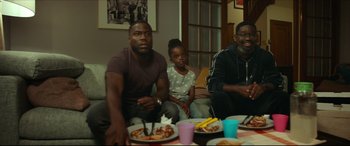Movie still from “Fatherhood” (2021), directed by Paul Weitz – A group of people sitting around a table with plates of food on top of it; Medium shot, Over the shoulder angle
