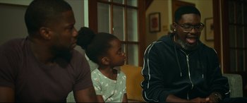 Movie still from “Fatherhood” (2021), directed by Paul Weitz – A little girl sitting next to two other people on a couch; Medium shot, Over the shoulder angle