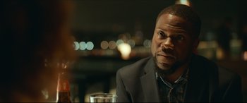 Movie still from “Fatherhood” (2021), directed by Paul Weitz – A person sitting at a table with a drink; Close Up shot, Over the shoulder angle