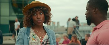 Movie still from “Fatherhood” (2021), directed by Paul Weitz – A person wearing a hat near a crowd of onlookers; Close Up shot, Over the shoulder angle