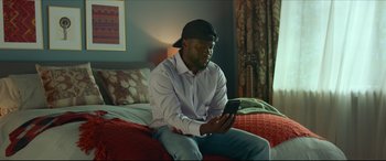Movie still from “Fatherhood” (2021), directed by Paul Weitz – A man sitting on a bed looking at a cell phone; Medium shot, Over the shoulder angle