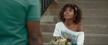 Movie still from “Fatherhood” (2021), directed by Paul Weitz – A woman sitting on steps holding a bouquet of flowers; Medium shot, Over the shoulder angle