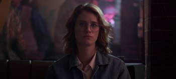 Movie still from “Black Mirror” (2011), created by Charlie Brooker – A woman with glasses is looking at the camera; Close Up shot, Low angle