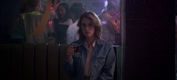 Movie still from “Black Mirror” (2011), created by Charlie Brooker – A woman holding a glass of beer while sitting at a bar; Medium shot, Over the shoulder angle