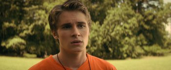 Movie still from “Fear Street: Part Two - 1978” (2021), directed by Leigh Janiak – A young man in an orange t - shirt looks at the camera; Close Up shot, Over the shoulder angle