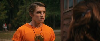 Movie still from “Fear Street: Part Two - 1978” (2021), directed by Leigh Janiak – A man in an orange t - shirt is standing outside; Close Up shot, Over the shoulder angle