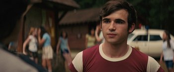 Movie still from “Fear Street: Part Two - 1978” (2021), directed by Leigh Janiak – A young man in a red and white t - shirt looks to his left; Close Up shot, Over the shoulder angle
