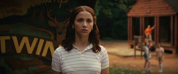 Movie still from “Fear Street: Part Two - 1978” (2021), directed by Leigh Janiak – A woman in a striped shirt is standing in a park; Close Up shot, Over the shoulder angle