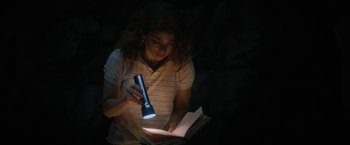 Movie still from “Fear Street: Part Two - 1978” (2021), directed by Leigh Janiak – A woman is reading a book with a flashlight; Medium shot, High angle