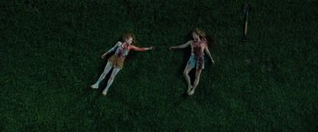 Movie still from “Fear Street: Part Two - 1978” (2021), directed by Leigh Janiak – Two young girls laying in the grass at night; Wide shot, Overhead angle
