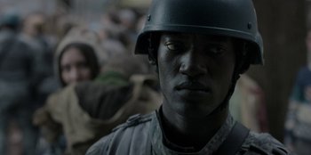 Movie still from “Black Mirror” (2011), created by Charlie Brooker – A man wearing a helmet is standing in front of a group of people; Close Up shot, Over the shoulder angle