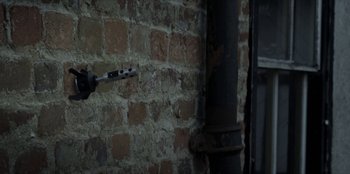 Movie still from “Black Mirror” (2011), created by Charlie Brooker – A man holding a drill next to a brick wall; Extreme Close Up shot, Low angle