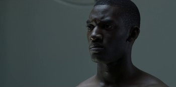Movie still from “Black Mirror” (2011), created by Charlie Brooker – A man's face in a dark room; Close Up shot, Low angle