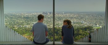 Movie still from “Friends with Benefits” (2011), directed by Will Gluck – A man and a woman sitting on top of a building looking out at a city; Wide shot, Over the shoulder angle