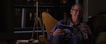 Movie still from “Friends with Benefits” (2011), directed by Will Gluck – An older man sitting in a chair holding a book; Medium shot, Over the shoulder angle